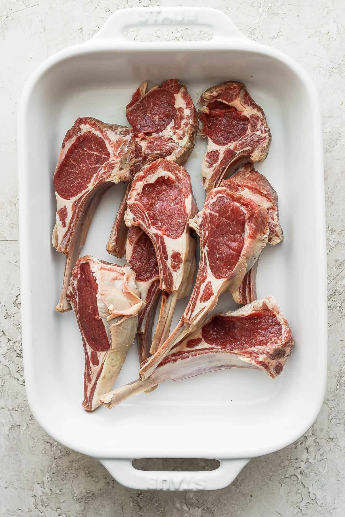 Raw lamb chops in a white baking dish.