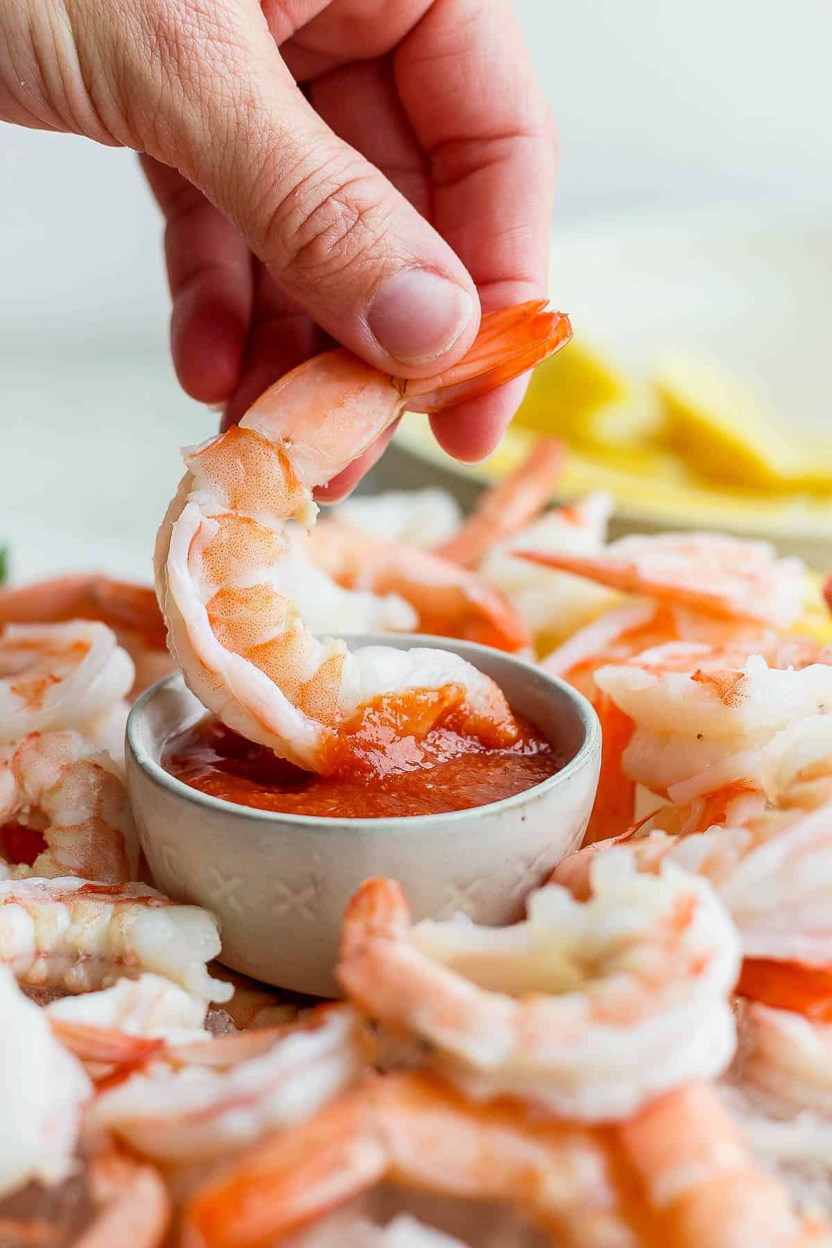 A hand scooping a shrimp into the small bowl of cocktail sauce.