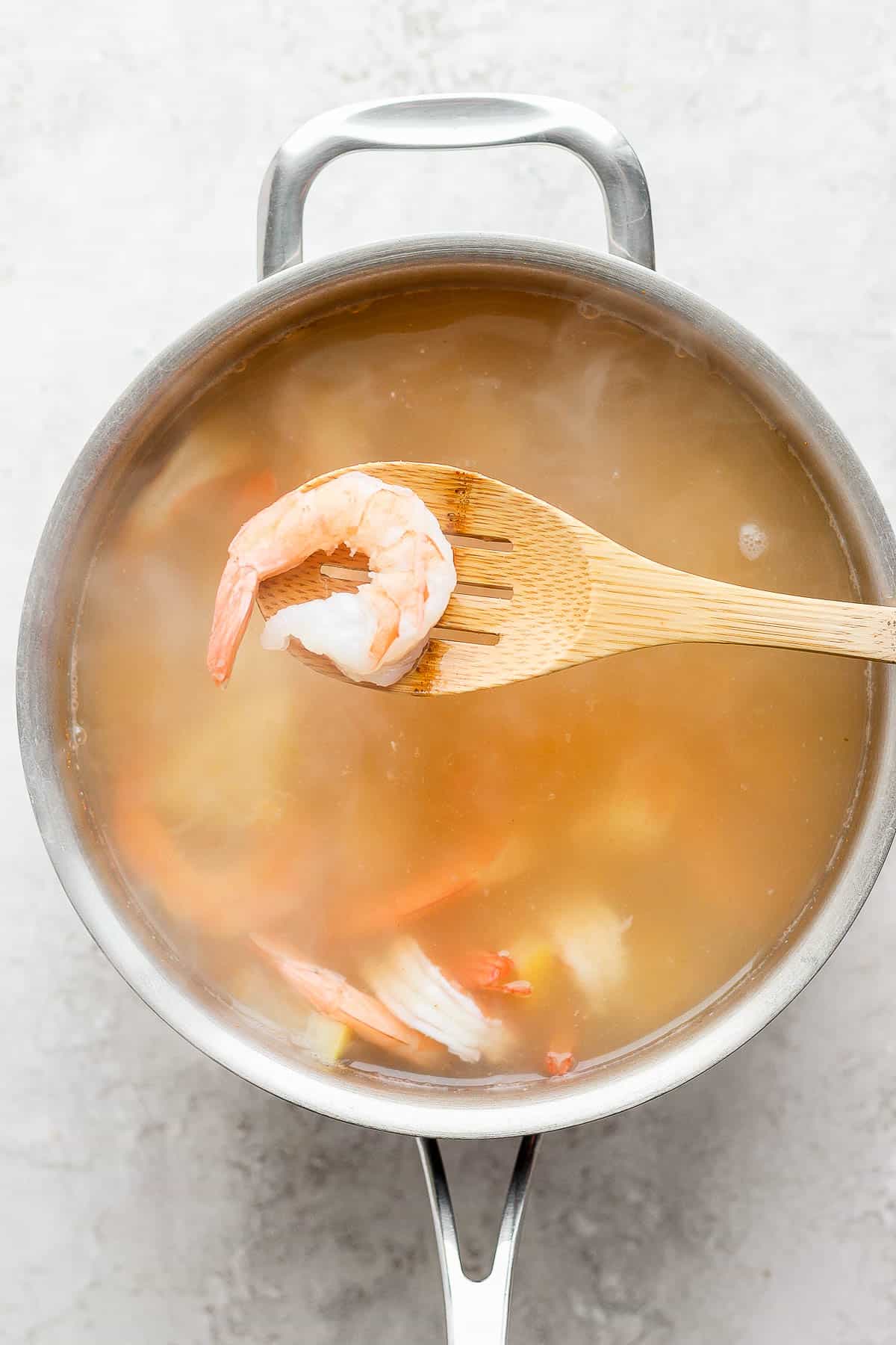 A fully cooked shrimp on a slotted wooden spoon hovering over the pot of seasoned water.