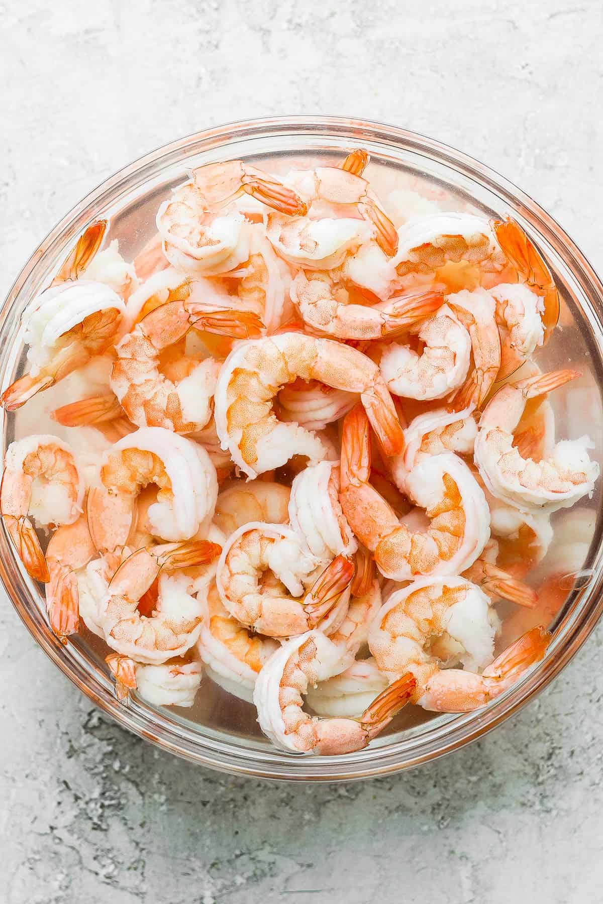 Fully cooked shrimp in a bowl of water and ice.