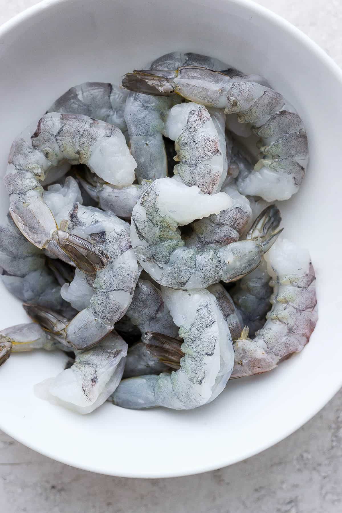Fresh shrimp with the tails on in a white bowl.