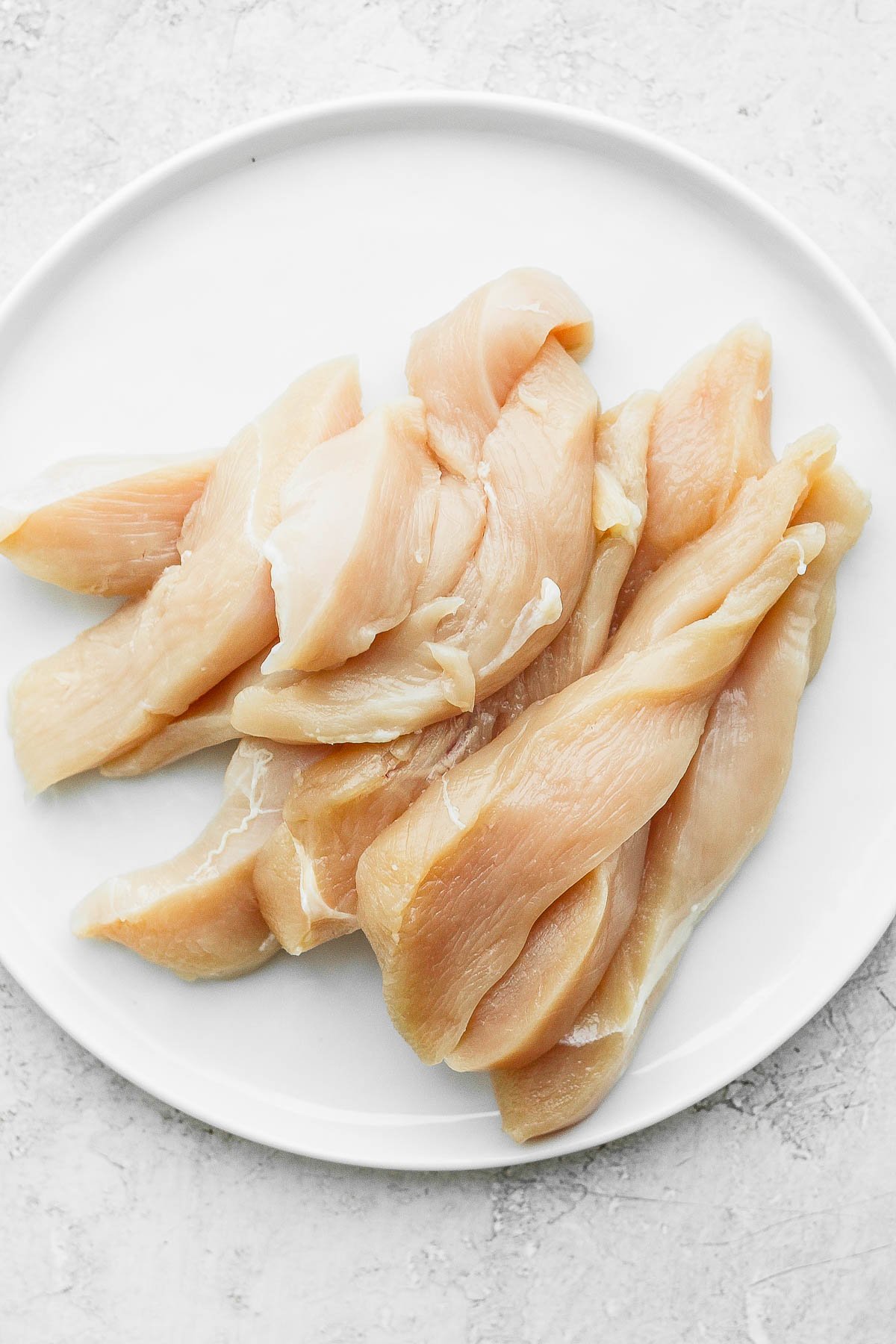 Raw chicken tenders on a white plate.