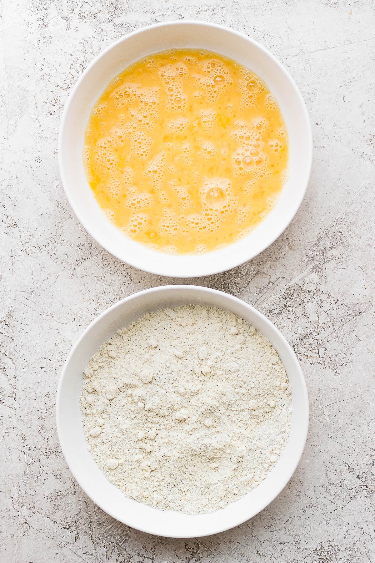 Two white bowls, one with egg wash and one with the dry ingredients.