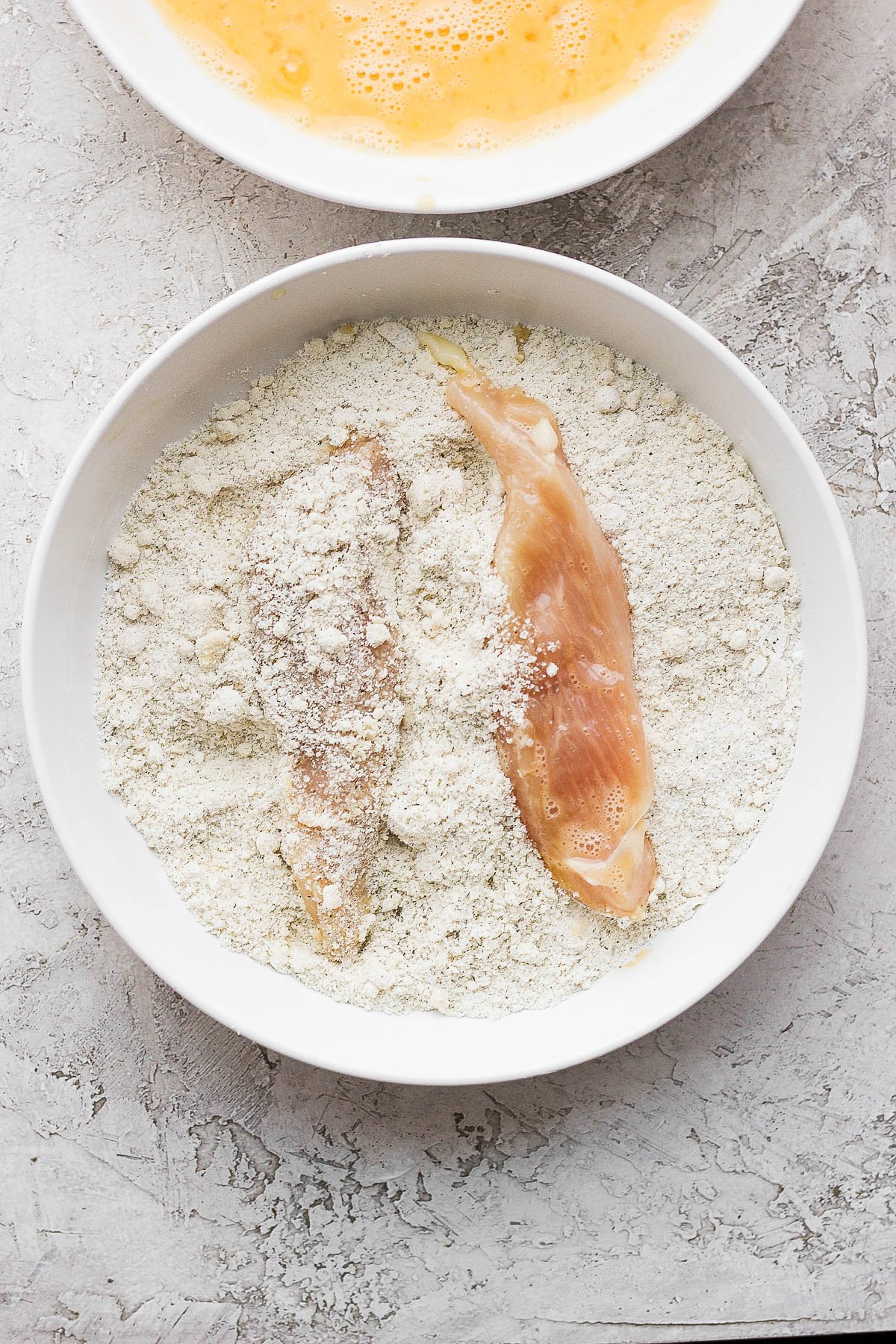 Chicken tenders in the almond flour mixture after being in the egg wash.