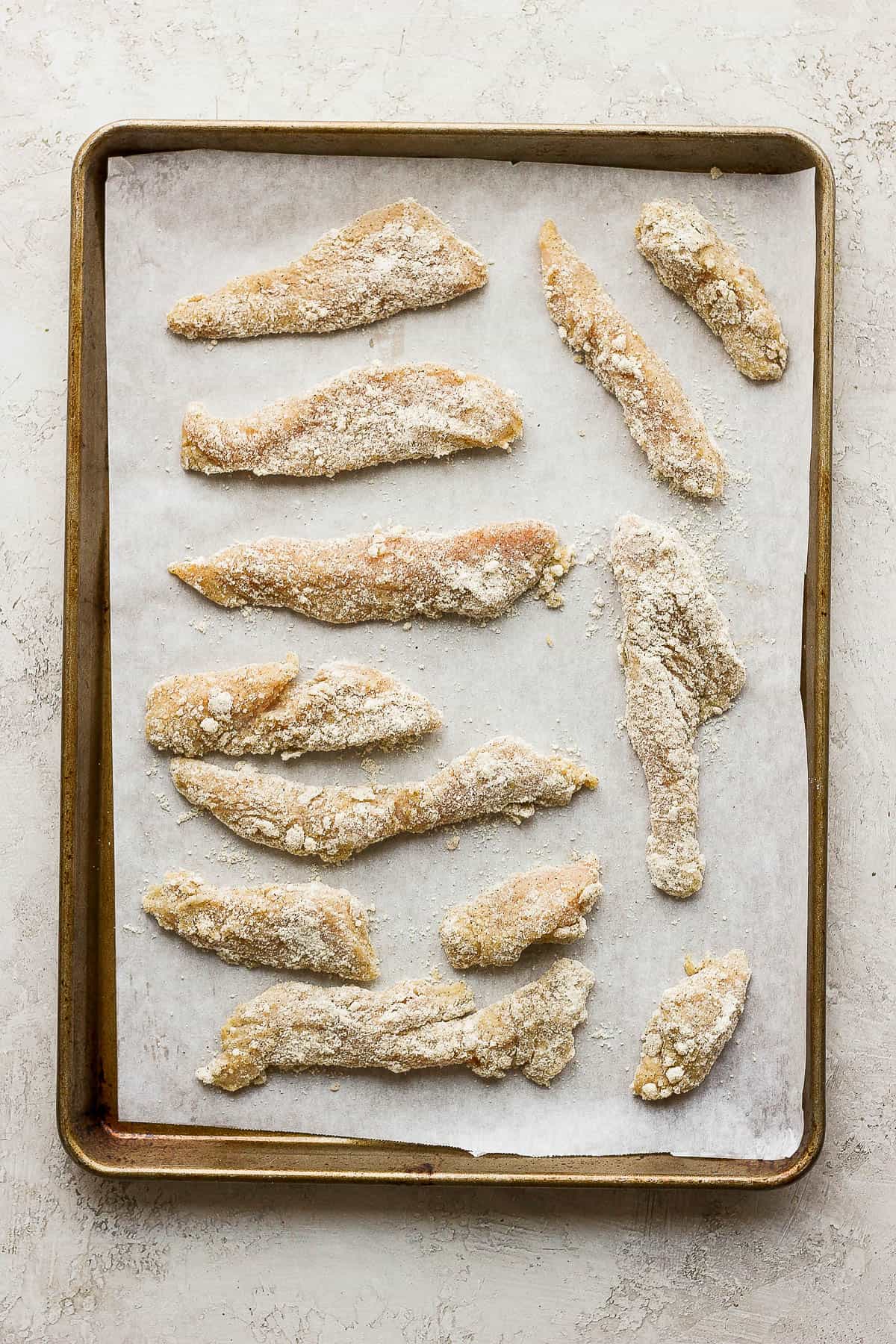 Chicken tenders on a parchment-lined baking sheet before baking.