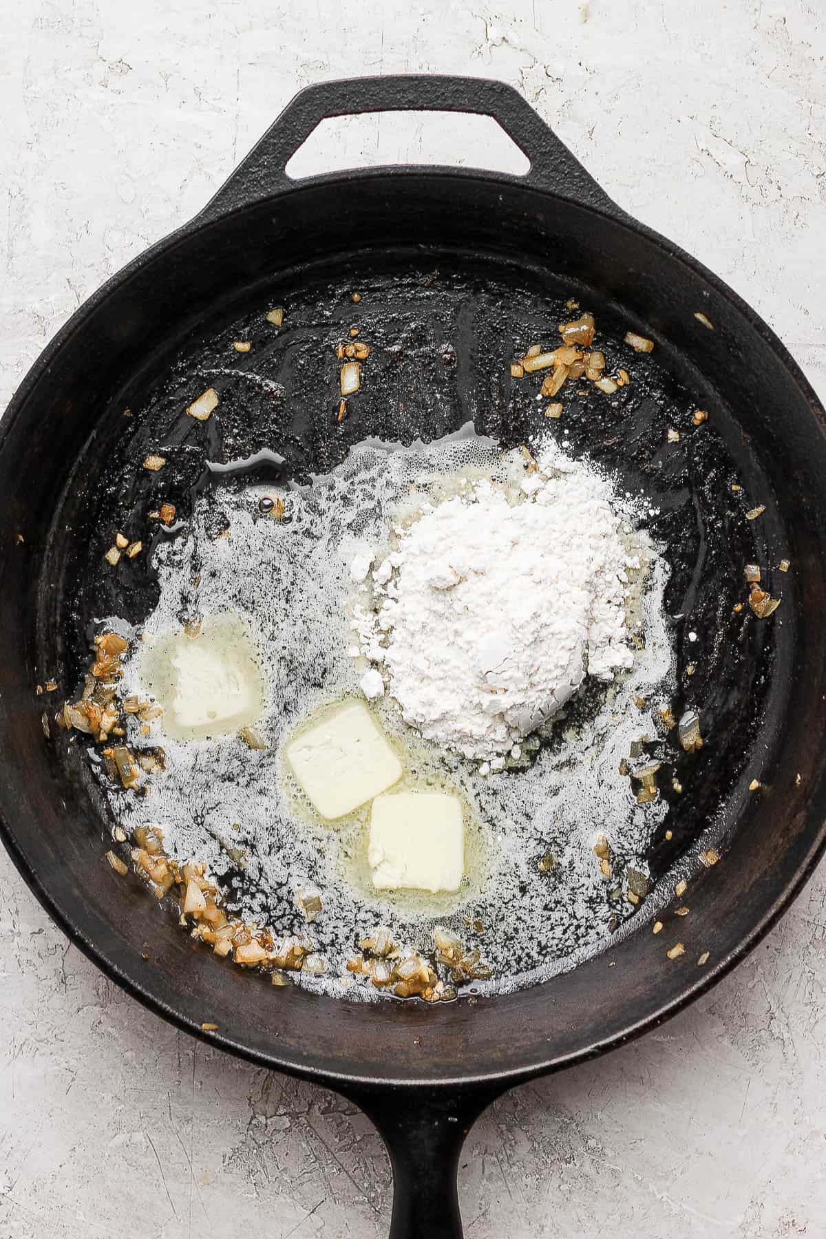 A cast iron skillet with three pats of melting butter and a flour in them middle.