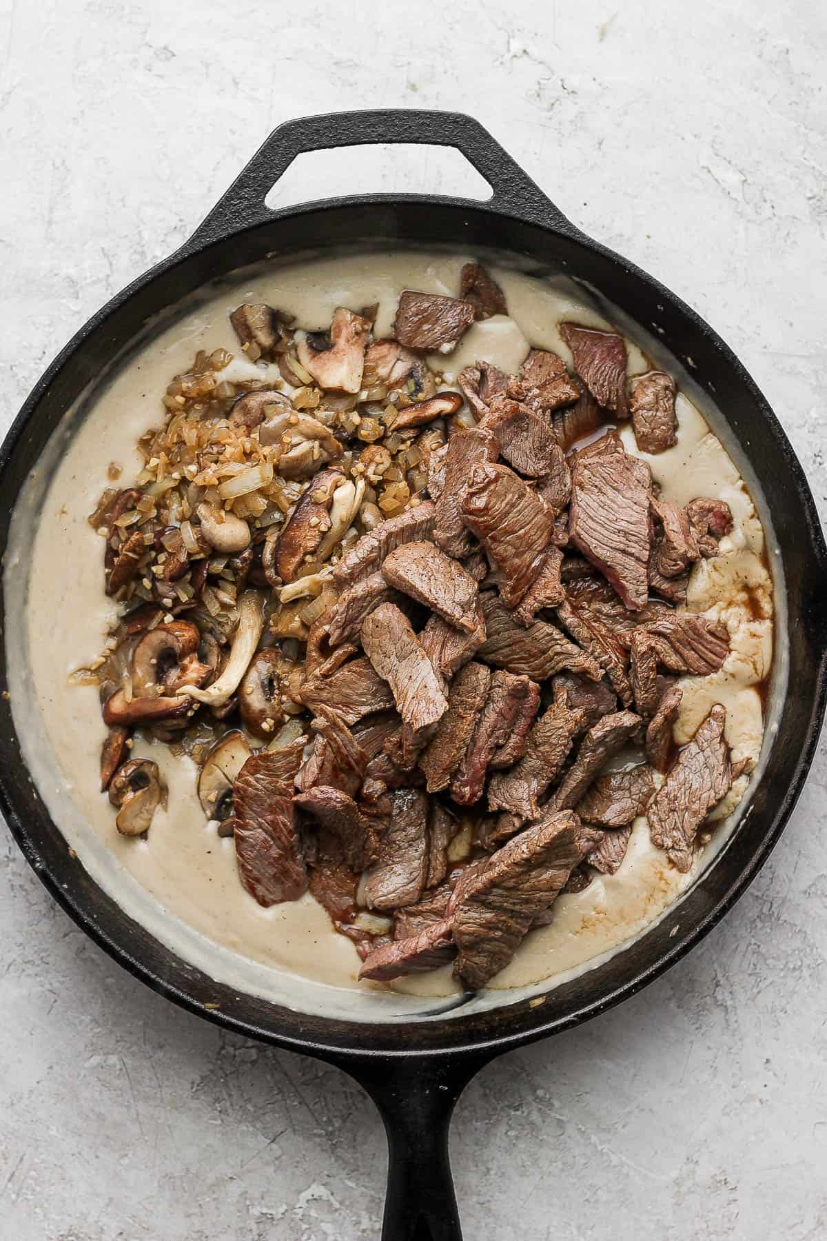 The seared two-inch strips of sirloin steak and mushroom, garlic, and onion mixture added back into the cast iron skillet that holds the roux.