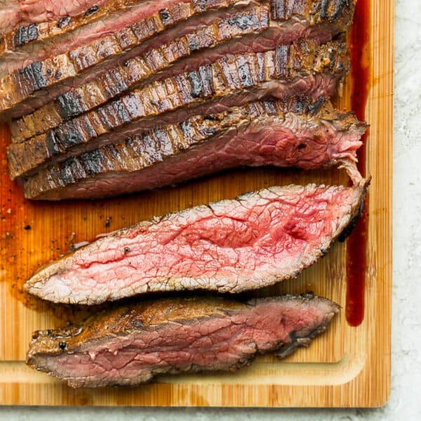 A cast iron flank steak on a cutting board cut into slices.