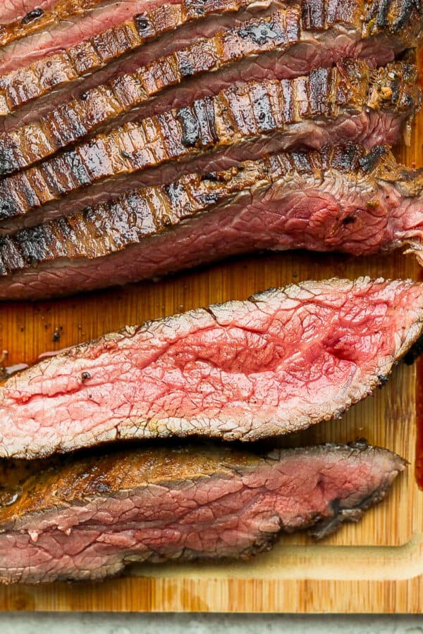 A cast iron flank steak on a cutting board cut into slices.