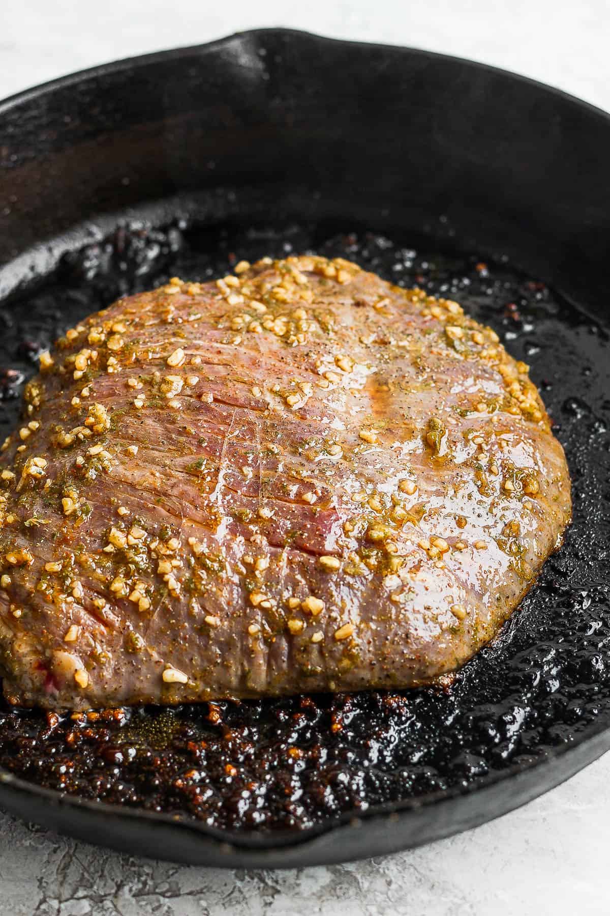 A partially cooked flank steak in a cast iron skillet.