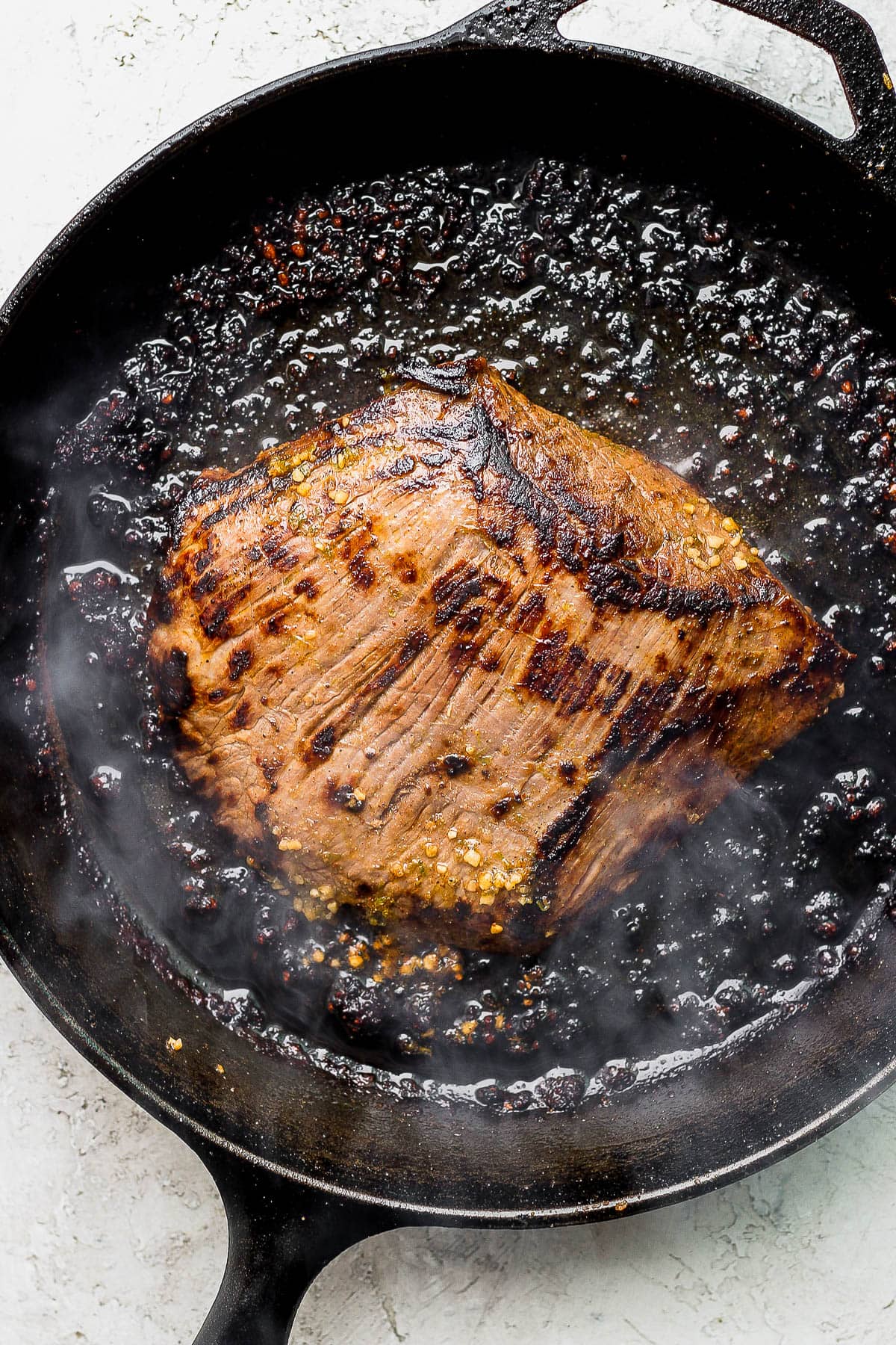 A seared flank steak in a cast iron skillet. 
