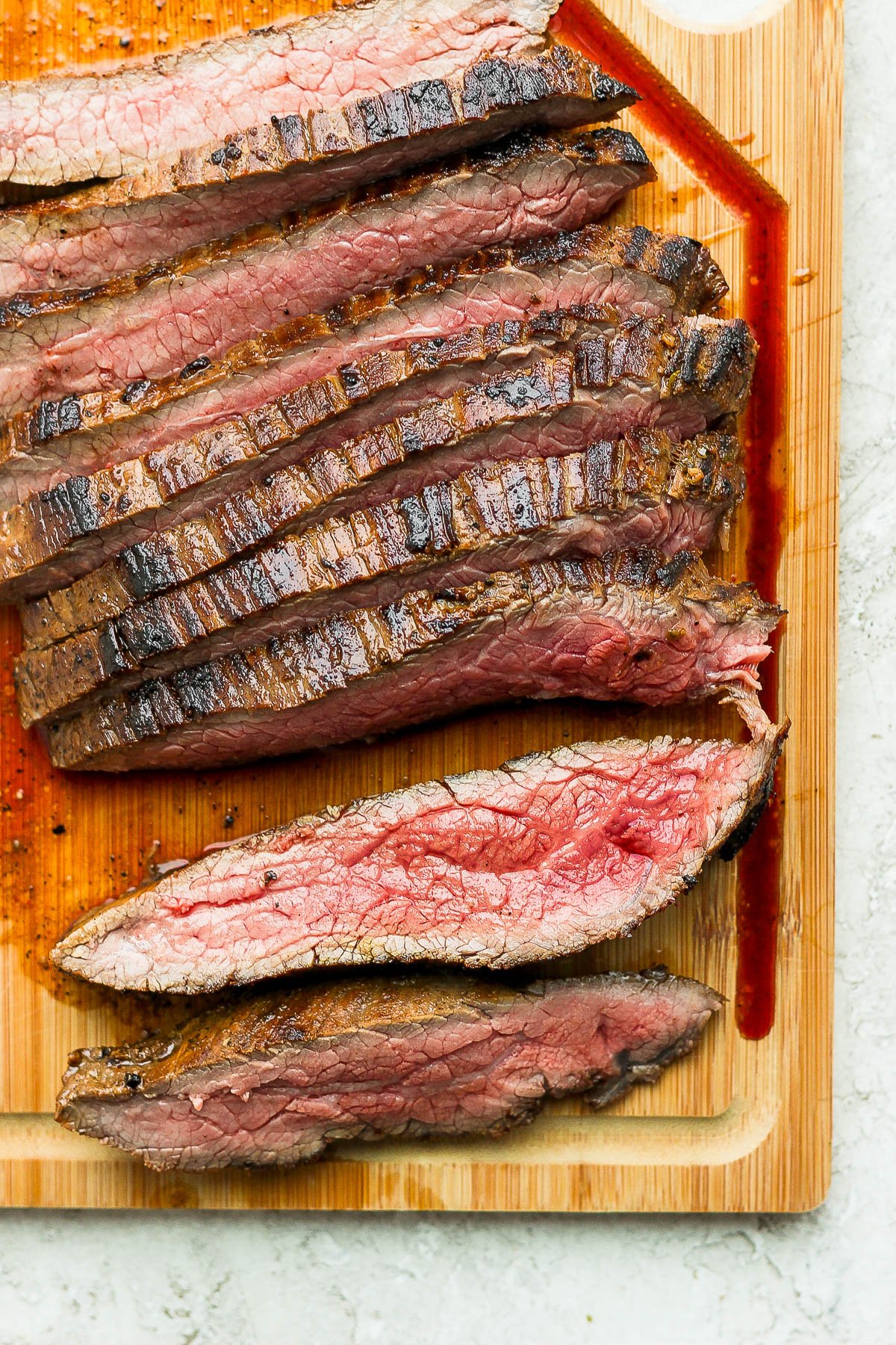 Cooked flank steak on a wood cutting board, sliced vertically against the grain of the meat fibers. 
