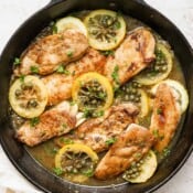 Cast iron skillet filled with chicken piccata with capers and lemon slices.