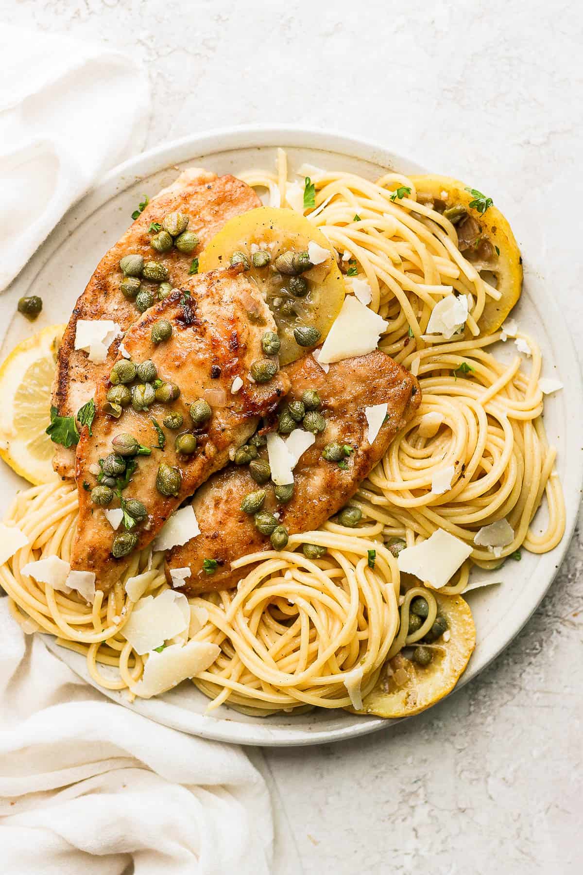 Chicken piccata served on top of spaghetti noodles with shaved parmesan sprinkled on top.