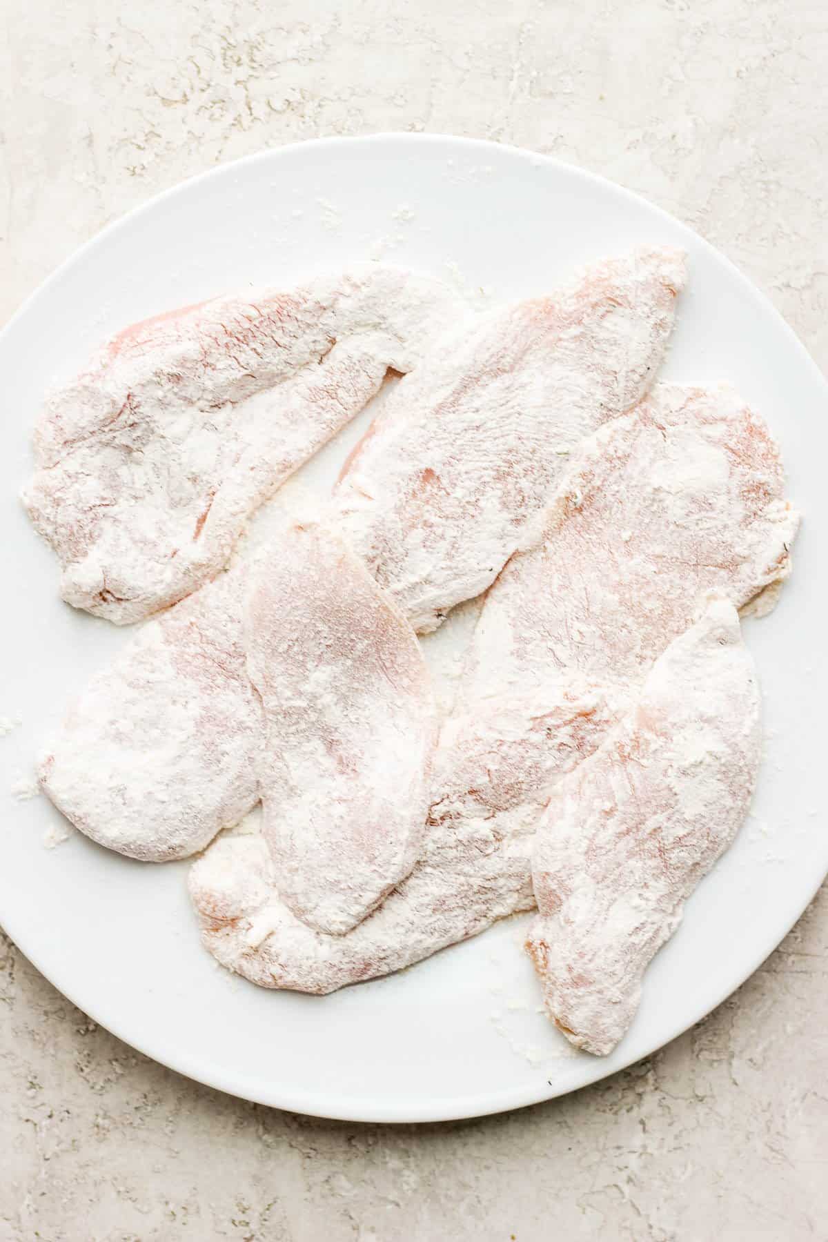 Seven flour and seasoning covered chicken cutlets on a clean plate.