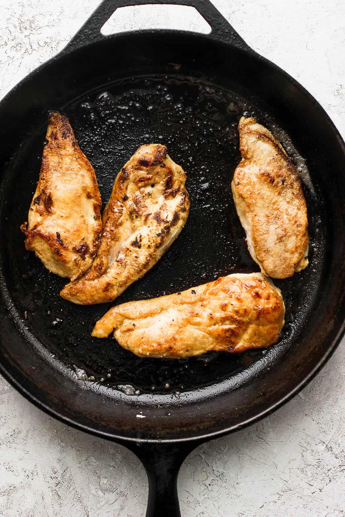 Four seared chicken cutlets on a cast iron skillet. 