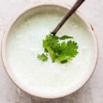 Bowl of cilantro lime sauce with a piece of cilantro on top and a spoon sticking out.