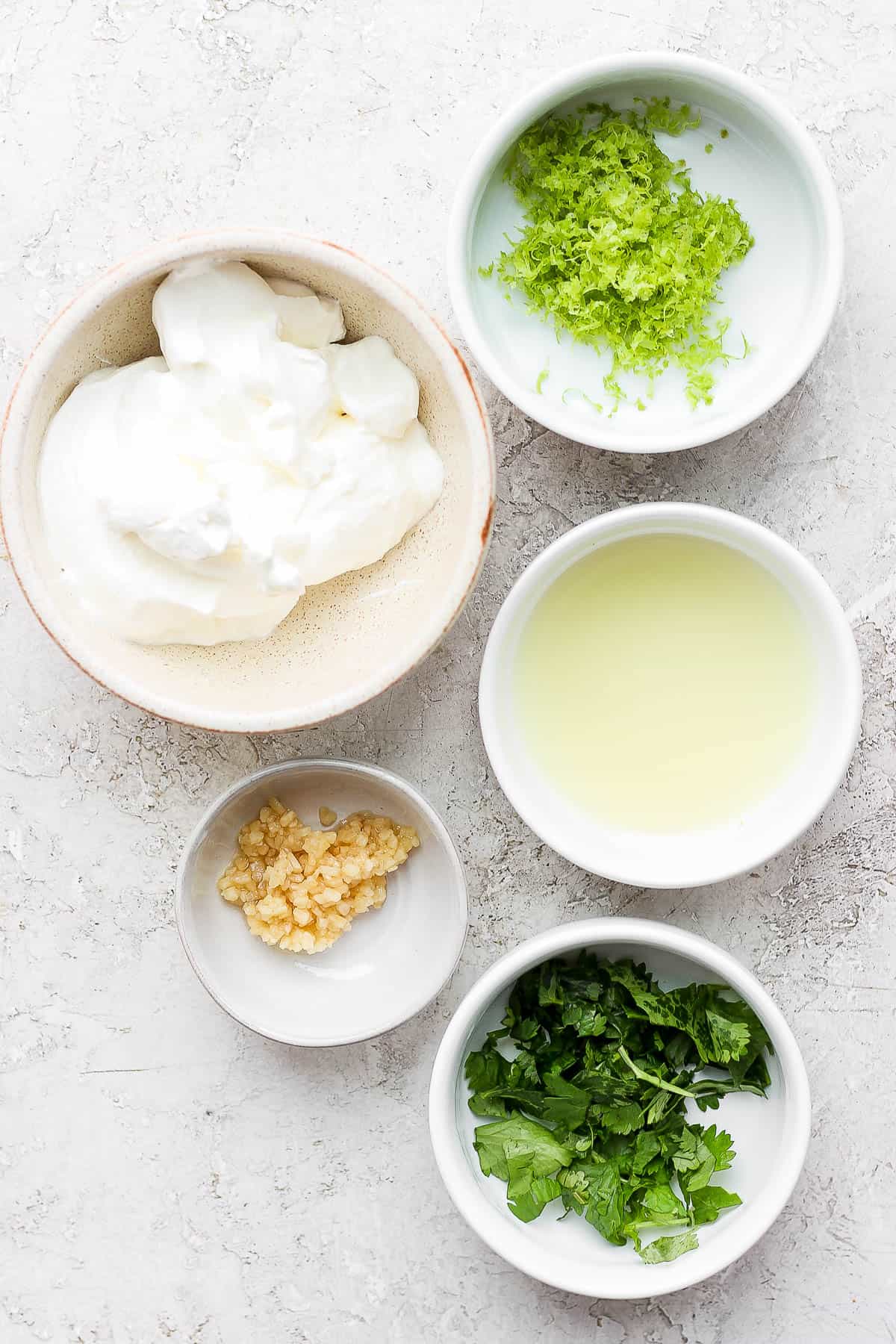 The prepped and measured ingredients all in individual bowls; lime zest, sour cream, lime juice, minced garlic, and cilantro.