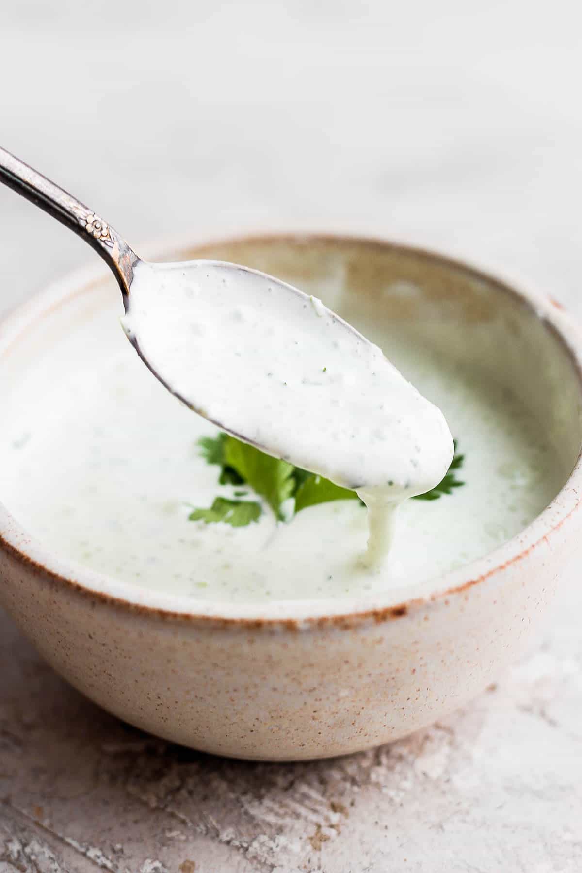 Cilantro lime sauce on a spoon hovering over a bowl of the sauce. 