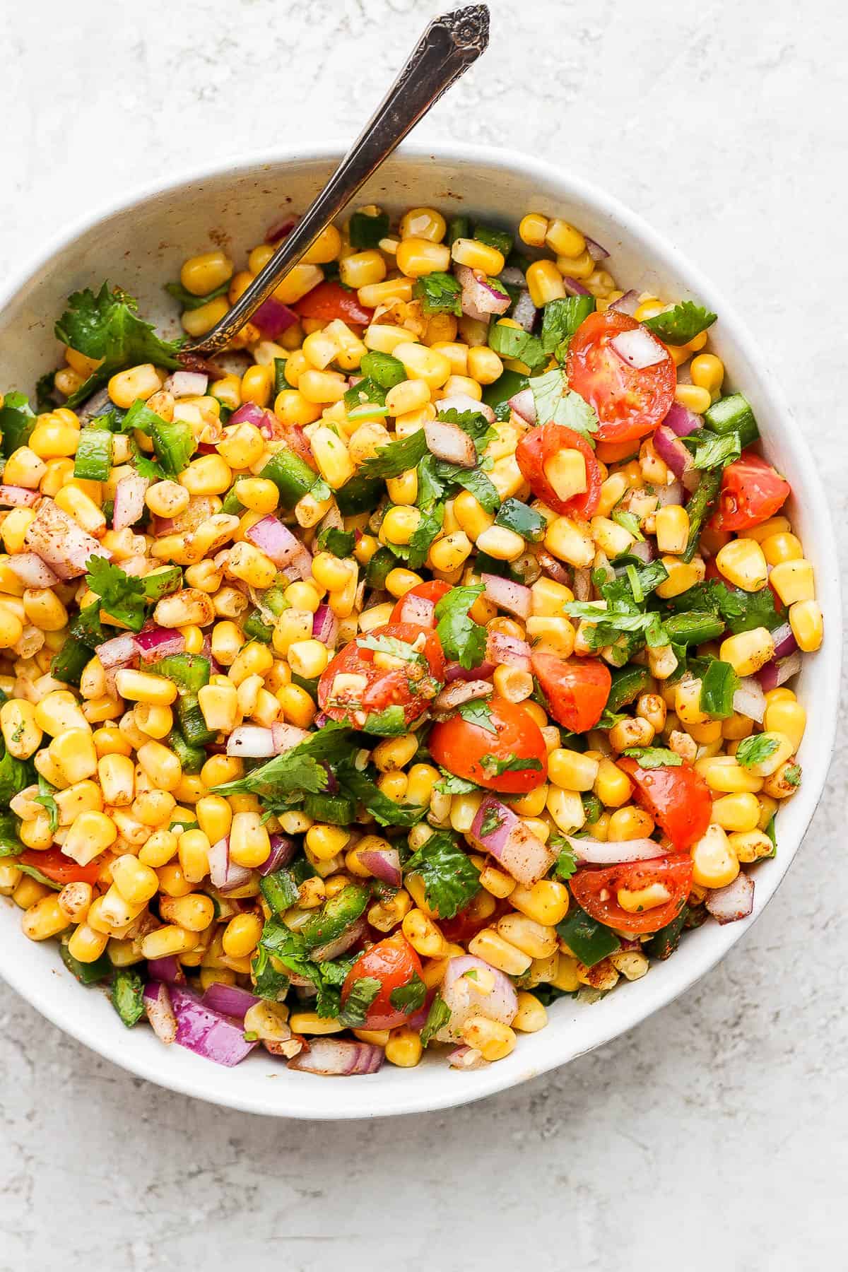 Completed corn salsa in a bowl with a spoon off to one side. 