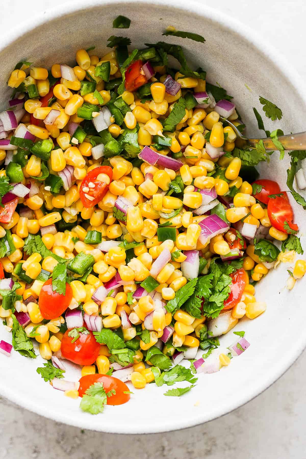 All of the salsa ingredients mixed together in a bowl with a spoon.