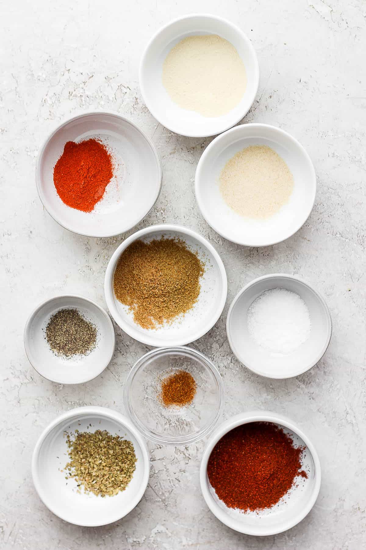 Small bowls, each with a measured spice required for the fajita seasoning; chili powder, kosher salt, paprika, onion powder, garlic powder, ground cayenne pepper, ground cumin, dried oregano leaves, ground black pepper.