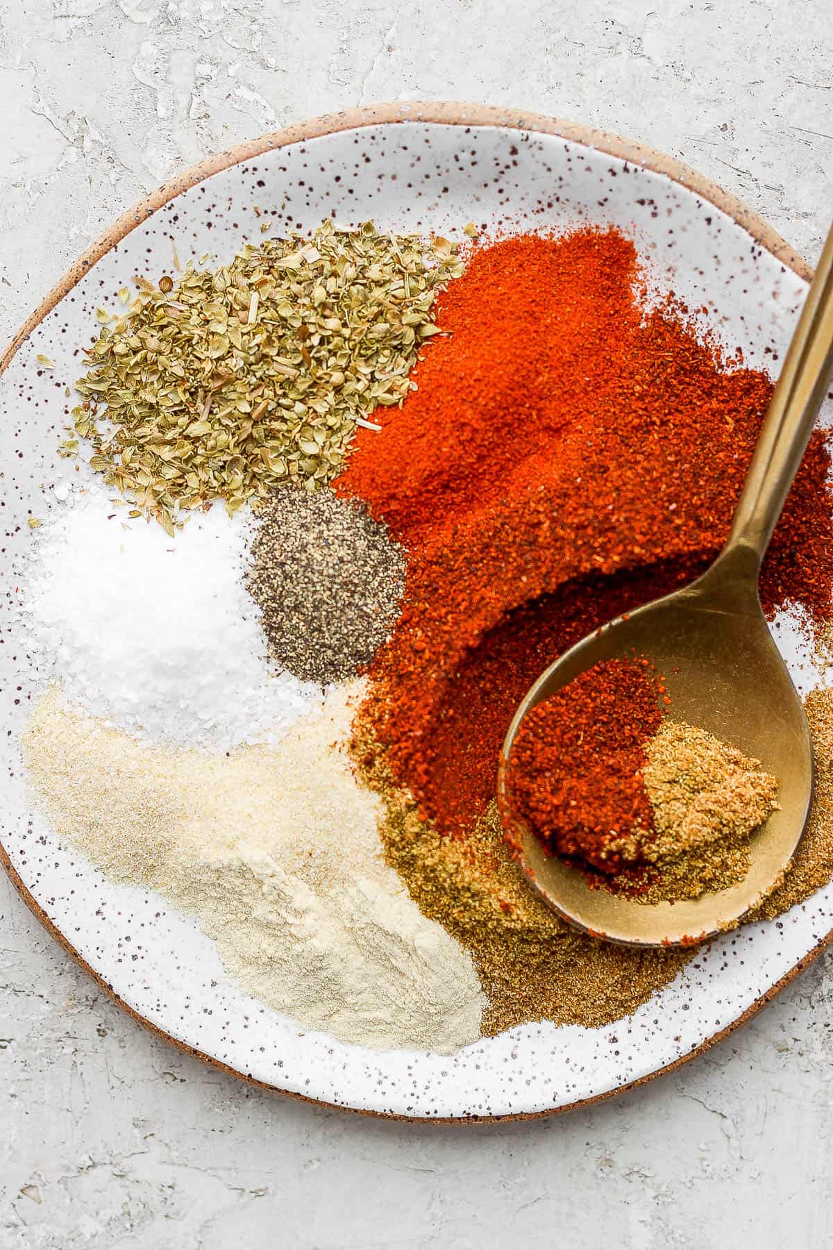 Fajita seasoning ingredients in a shallow bowl with a golden spoon.