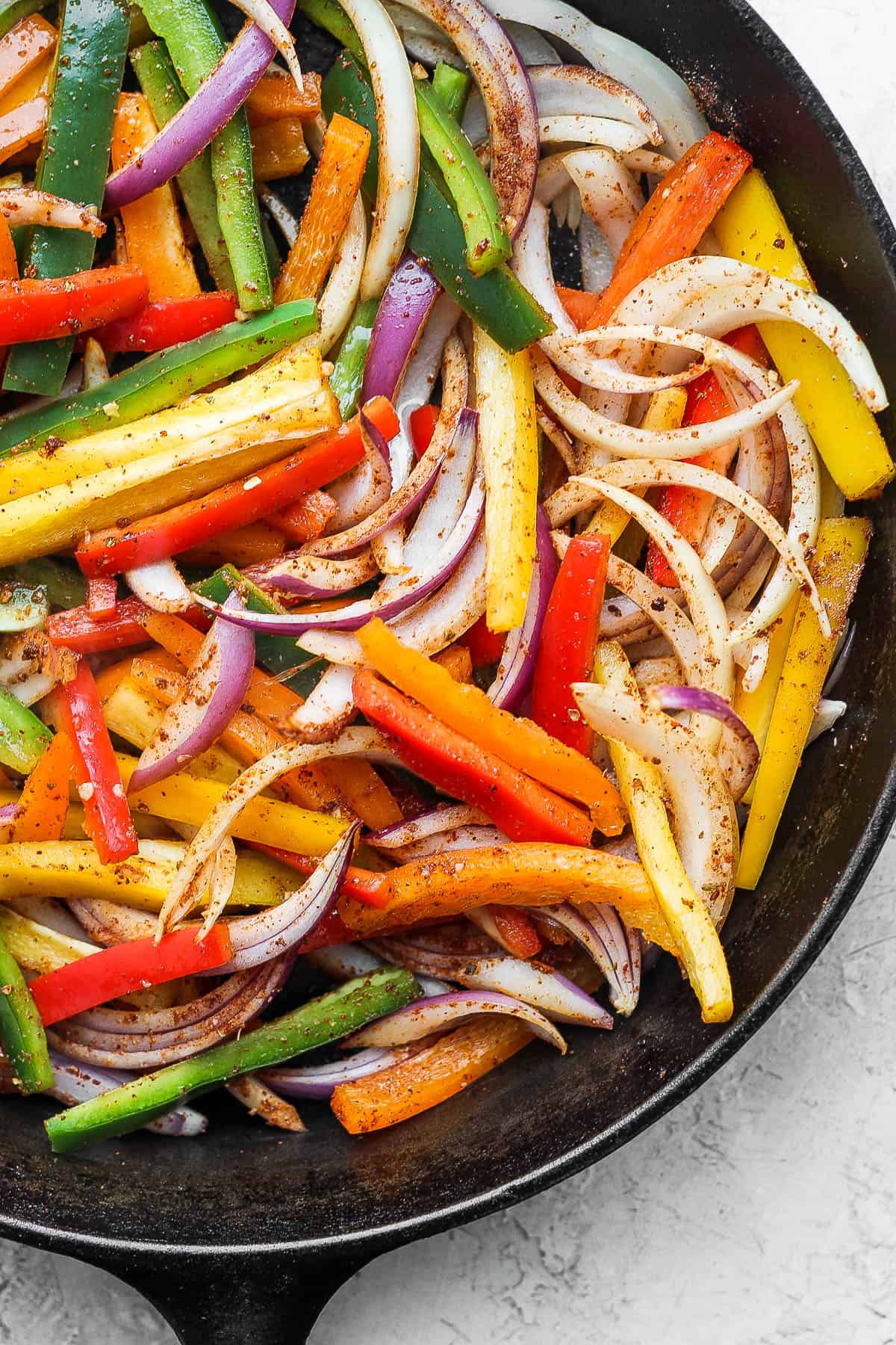 Fajita seasoning thoroughly coating sliced bell peppers, onion, and red onion in a cast iron skillet. 