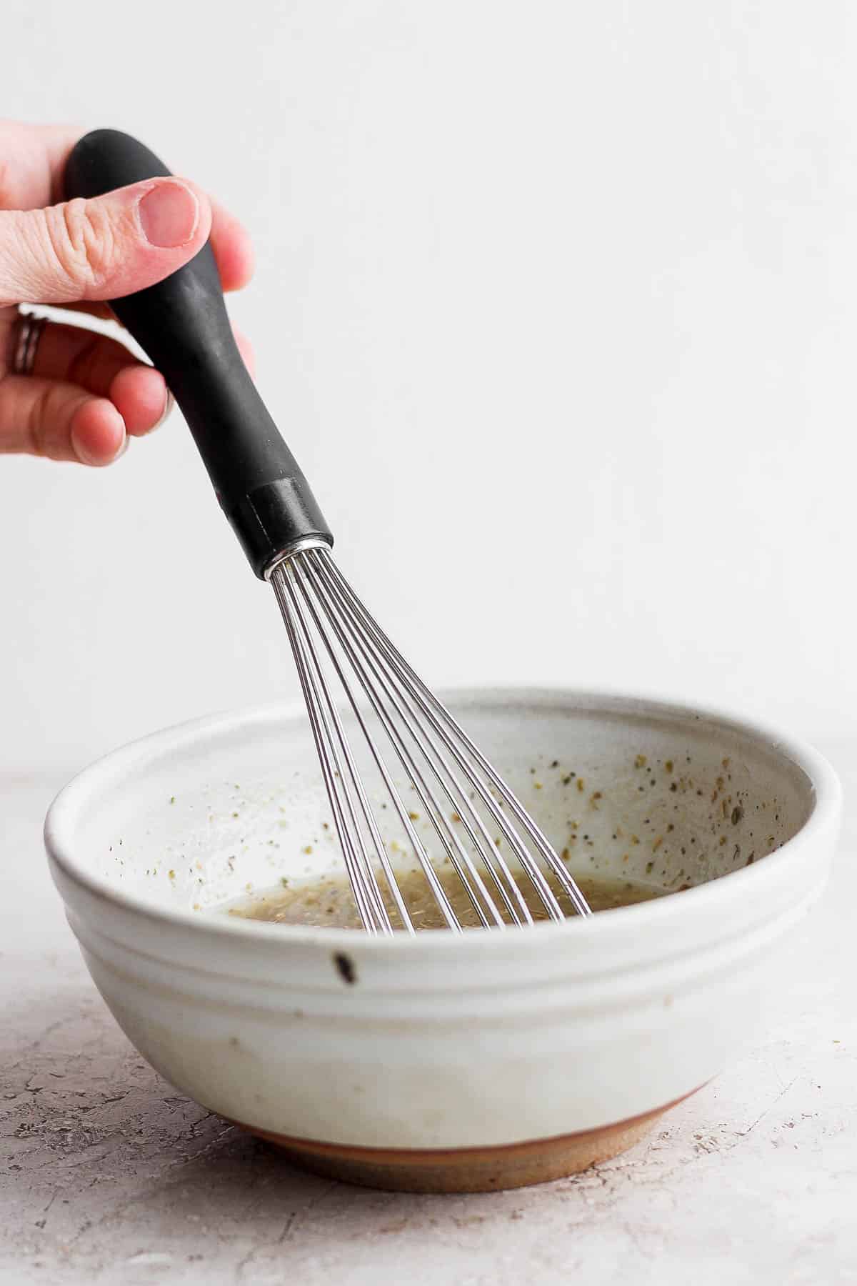 A hand holding a whisk in the small mixing bowl holding the marinade ingredients. 