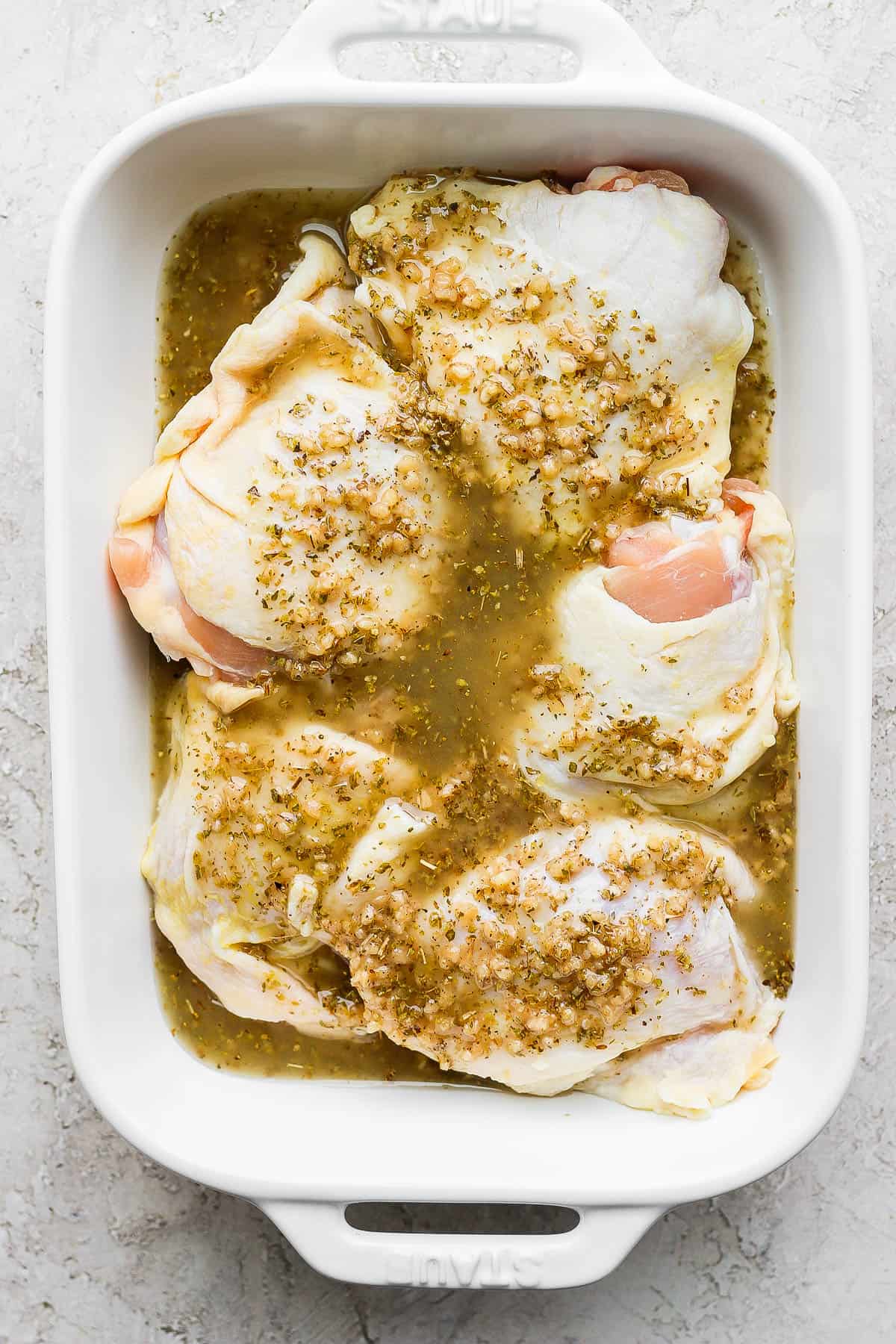 Bone-in, skin on chicken thighs in a casserole dish covered in greek marinade.