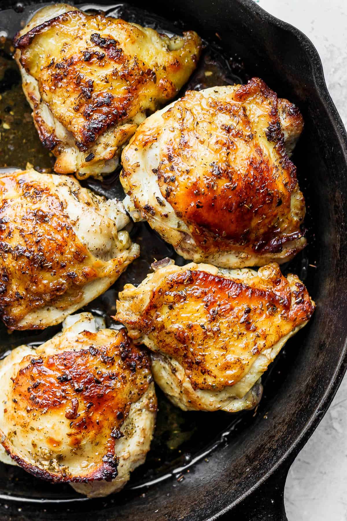 Marinated chicken thighs searing in a cast iron skillet.