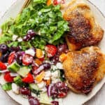 Plate of two greek chicken thighs with a cucumber greek salad.