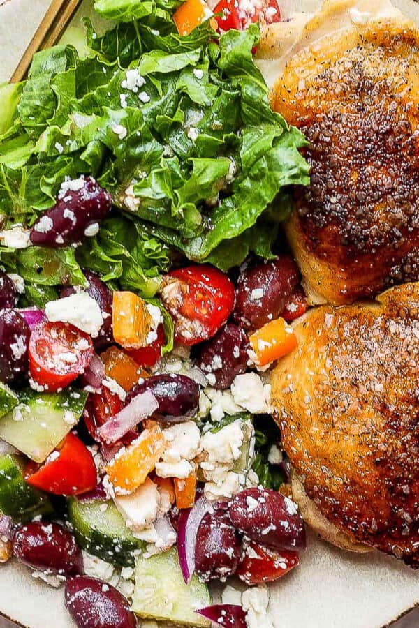 Plate of two greek chicken thighs with a cucumber greek salad.