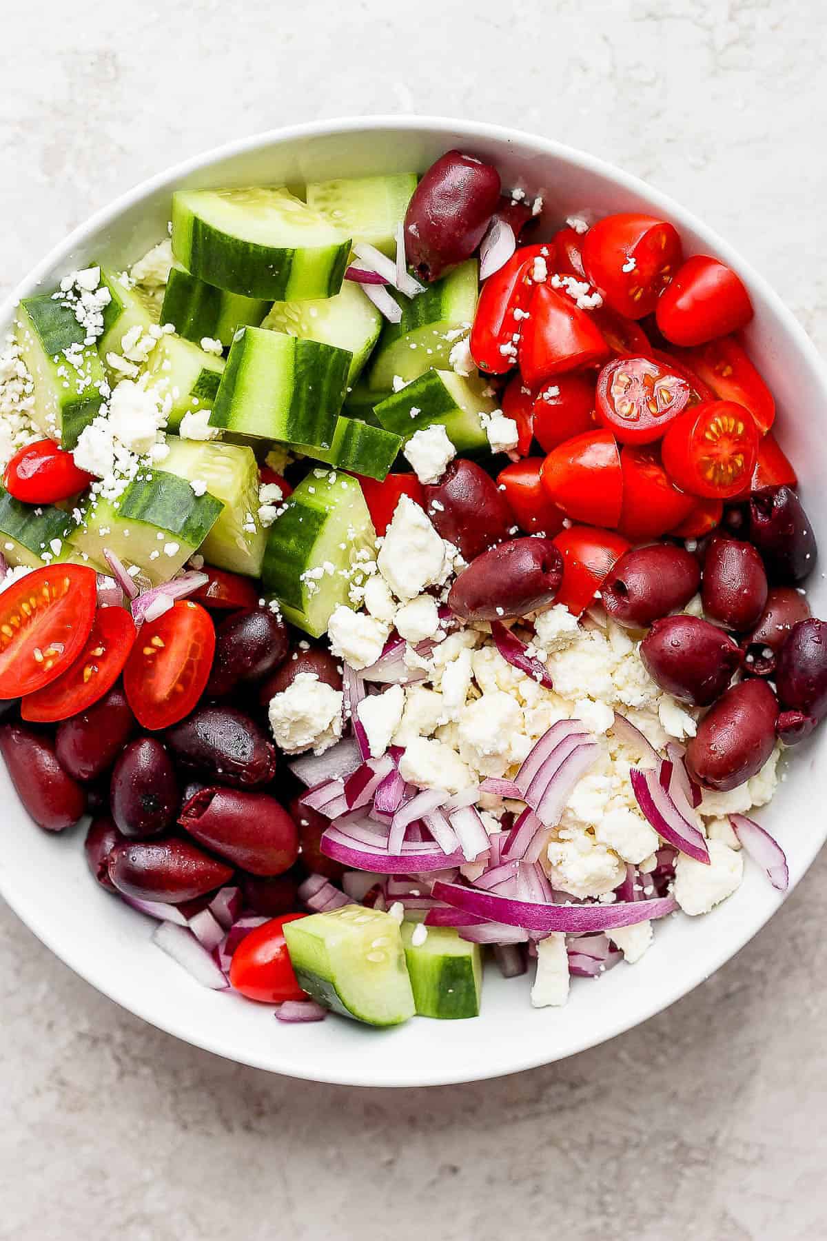 A greek cucumber salad in a bowl containing chopped cucumbers, cherry tomatoes, red onion, feta, and olives. 