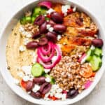 A hummus bowl with cucumber, kalamata olives, farro, chicken and hummus.