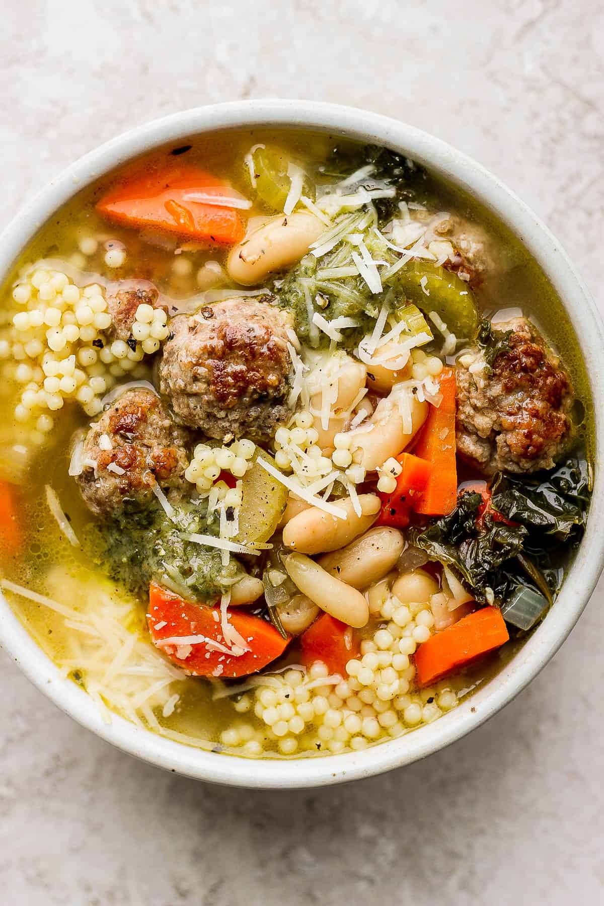 A bowl of Italian wedding soup with basil pesto and parmesan cheese on top.