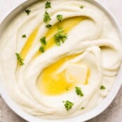 Bowl of mashed cauliflower with fresh parsley and melted butter.