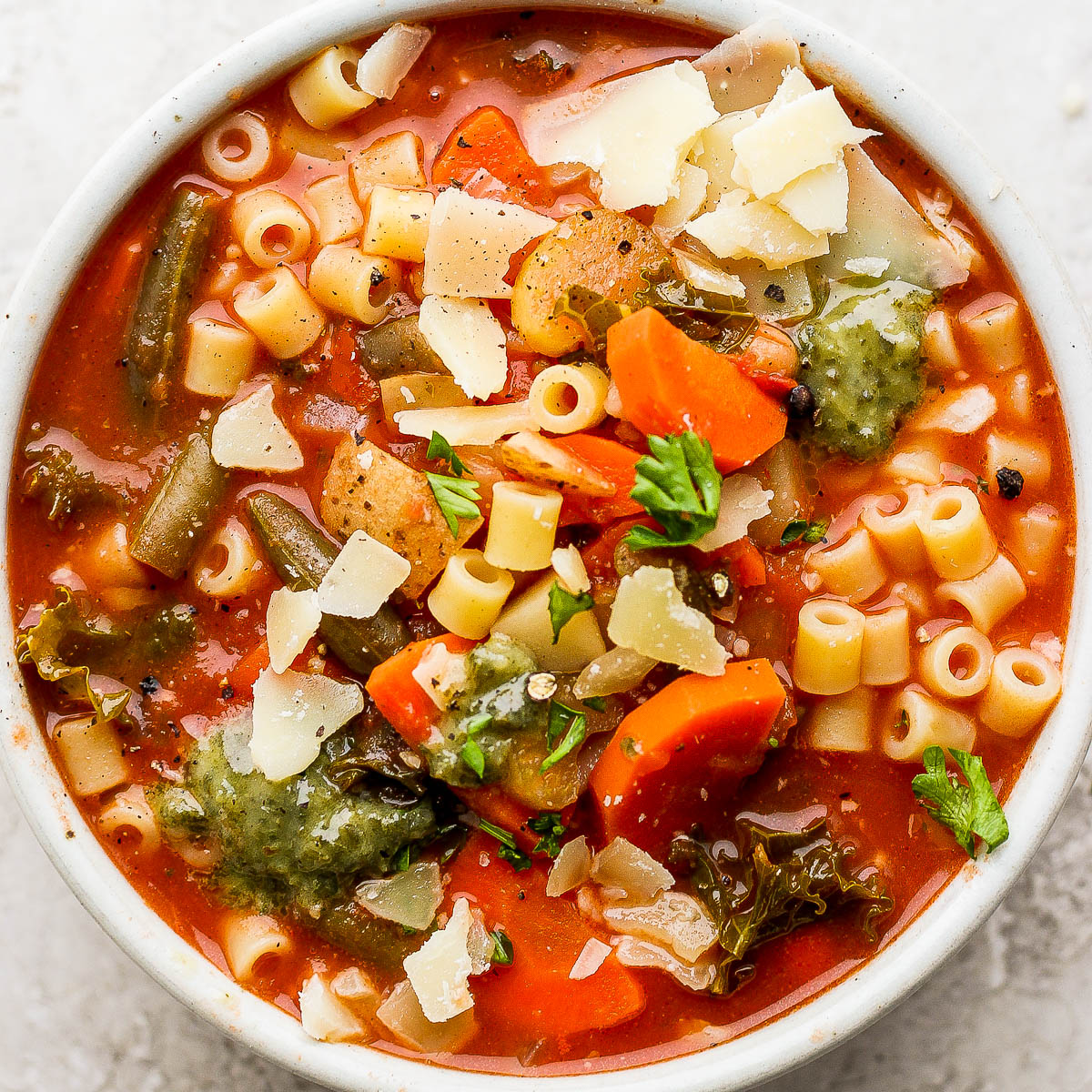 Bowl of minestrone soup with pasta and parmesan cheese on top.