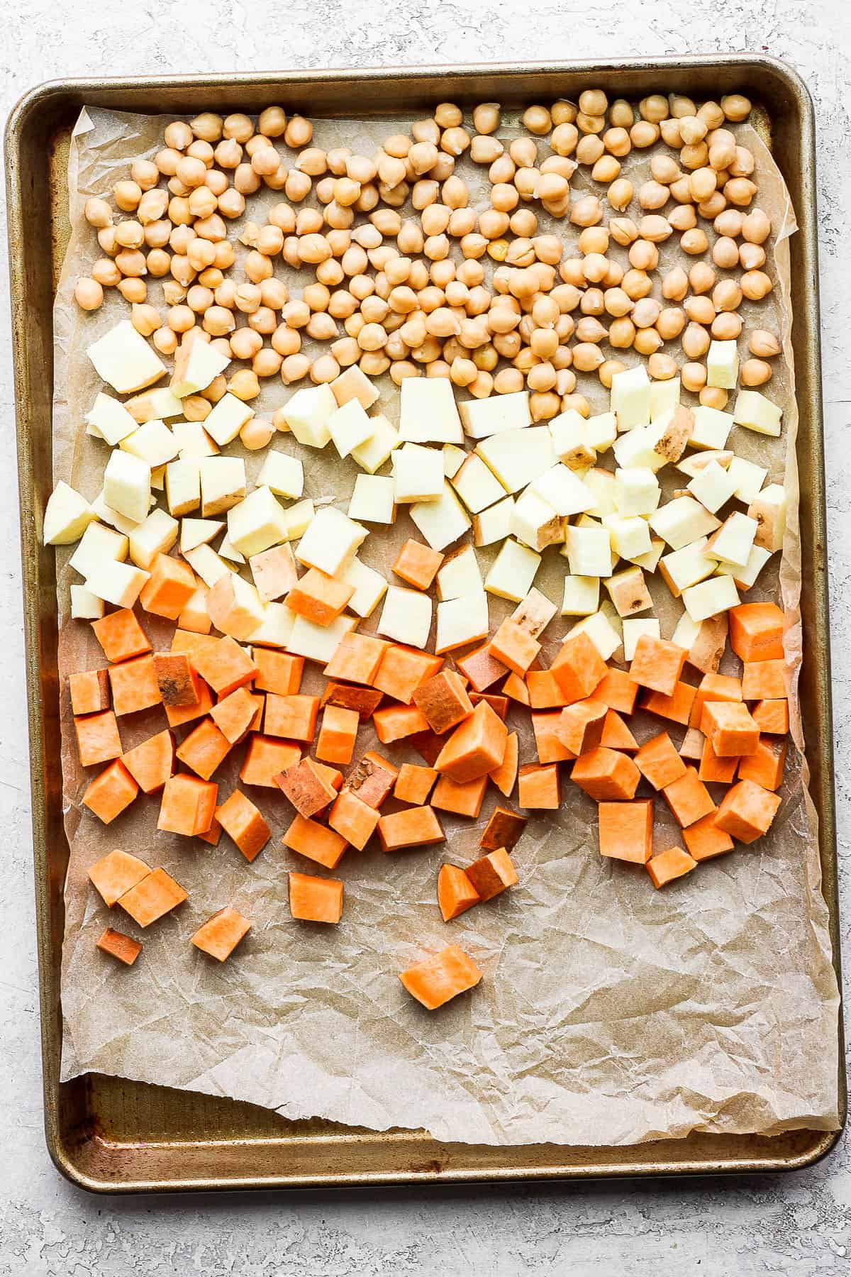 Chickpeas, cubed white sweet potato, and cubed yams on a baking sheet lined with parchment paper. 