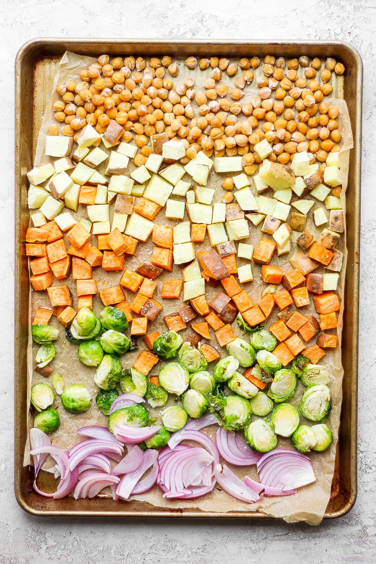 The same baking sheet, now with noticeably roasted yams, sweet potato and chickpeas.  Halved brussels sprouts and sliced red onion have been added to one side of the pan.