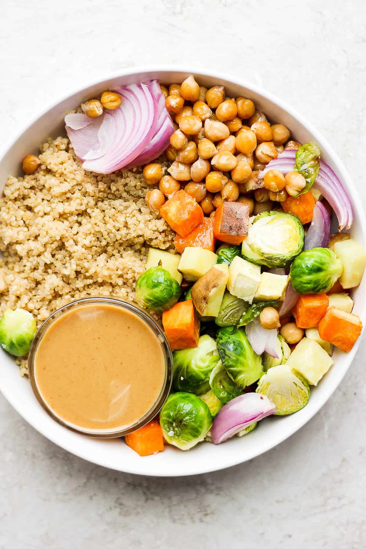 A bowl holding coconut quinoa and roasted veggies.  A small bowl of peanut sauce is nestled into the bowl off to one side. 