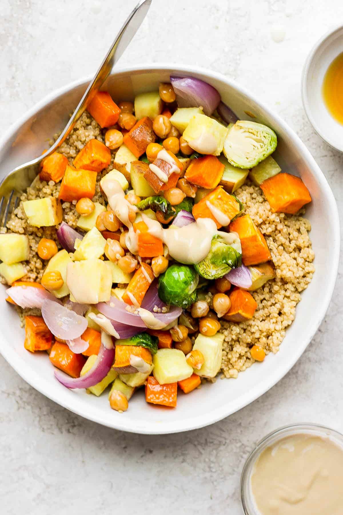 A quinoa bowl with coconut quinoa on the bottom topped with roasted brussels sprouts, chickpeas, red onion, yams, sweet potatoes all drizzled with peanut sauce. 