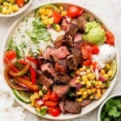 A steak fajita bowl with steak, veggies, cilantro lime rice, corn salsa, sour cream, guacamole and tomatoes.