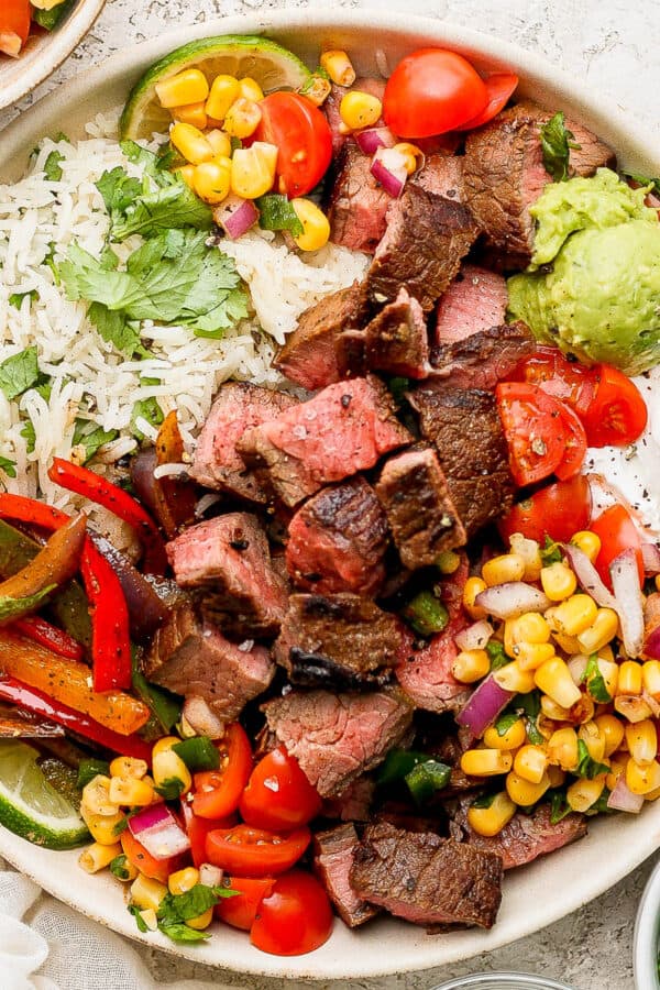 A steak fajita bowl with steak, veggies, cilantro lime rice, corn salsa, sour cream, guacamole and tomatoes.