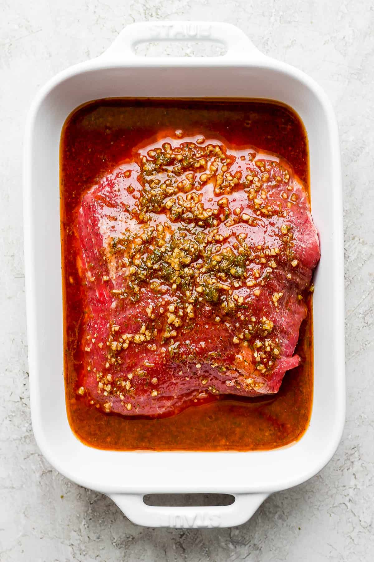 Steak fajita marinade in a shallow baking dish with the steak.