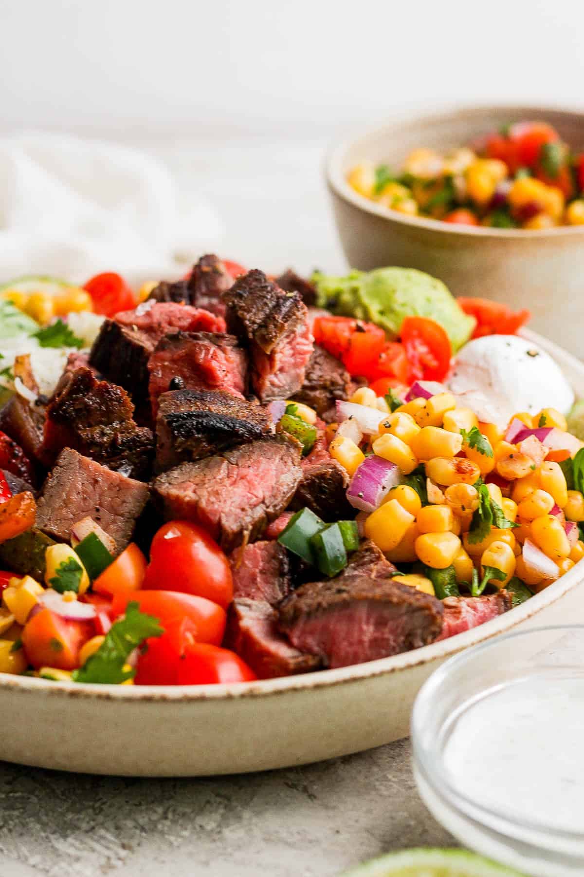 The steak fajita bowl with a bowl of corn salsa next to it.