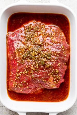 A ceramic dish with aa flank steak covered in a fajita marinade.