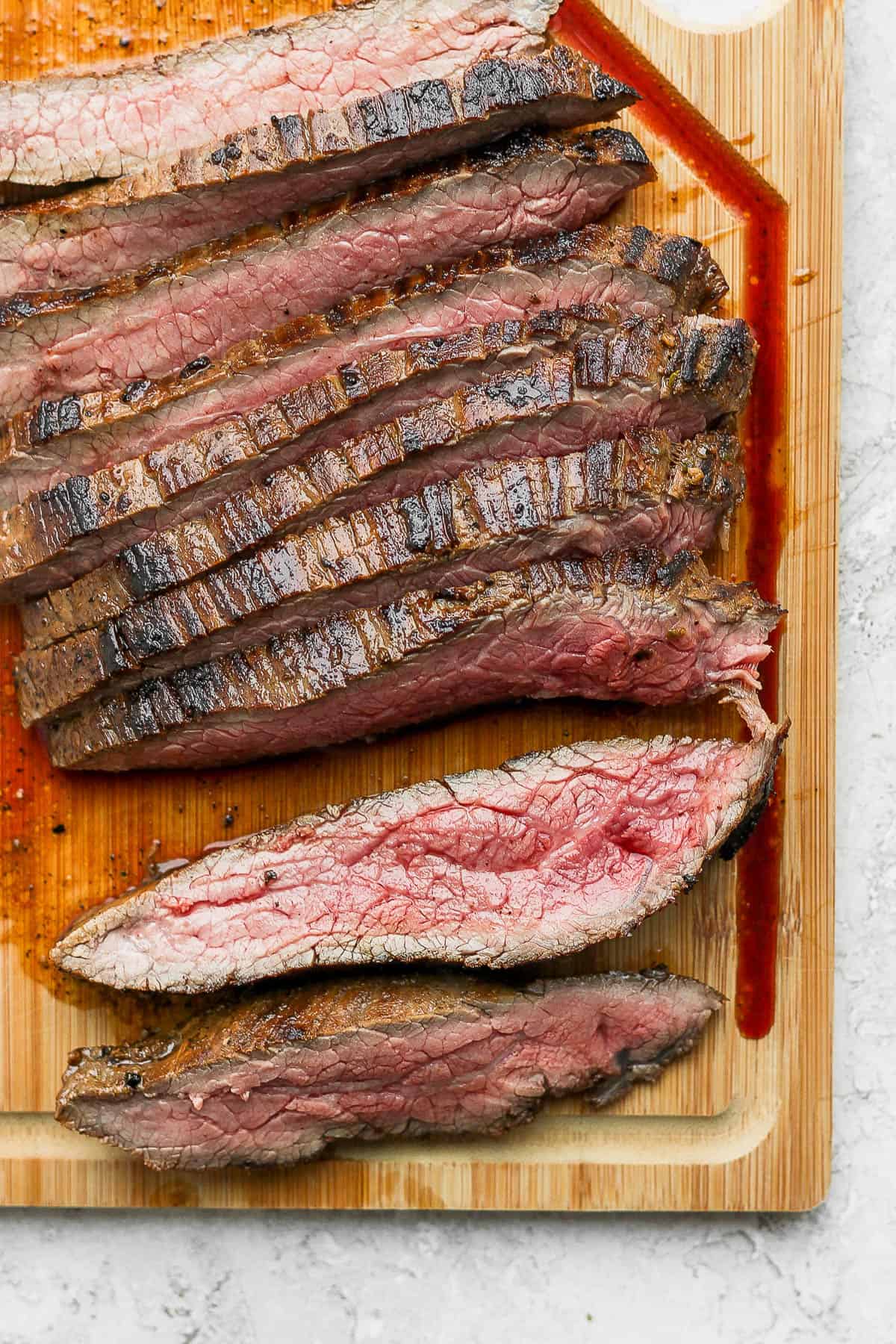 Marinated and cooked flank steak on a cutting board.