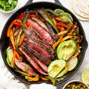 A cast iron skillet filled with steak fajitas with veggies, steak and avocado.