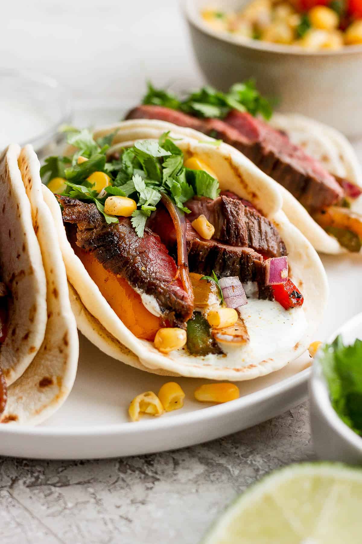 A steak fajita on a plate with fresh cilantro and corn salsa.